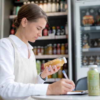 Szef kuchni lub kucharz odkładający warzywa lub produkty spożywcze do pojemników GN lub specjalnego regału, z widocznymi etykietamidatami.